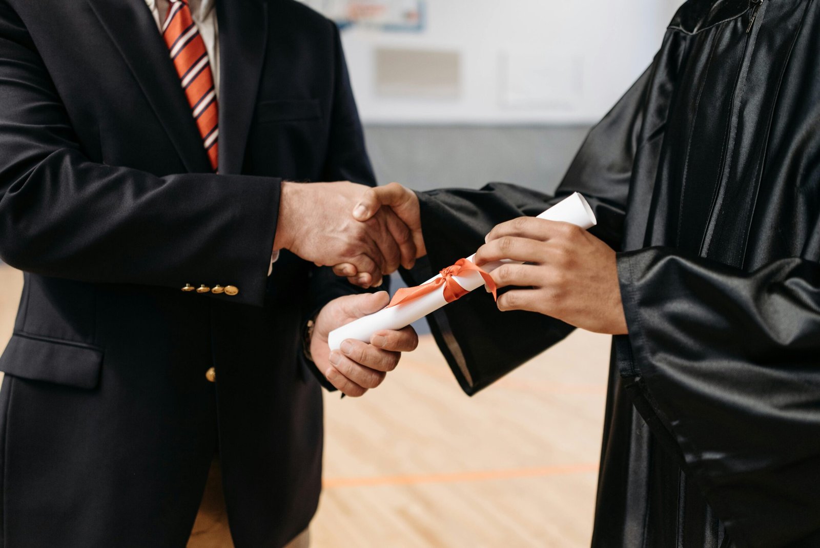 Close-up of a graduate receiving diploma during a graduation ceremony handshake.